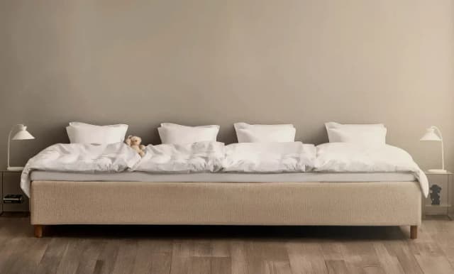 Wide beige family bed made up with white duvets and four pillows in a row