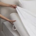 Hands fitting the white sheet over a quilted foam bolster at the edge of the bed