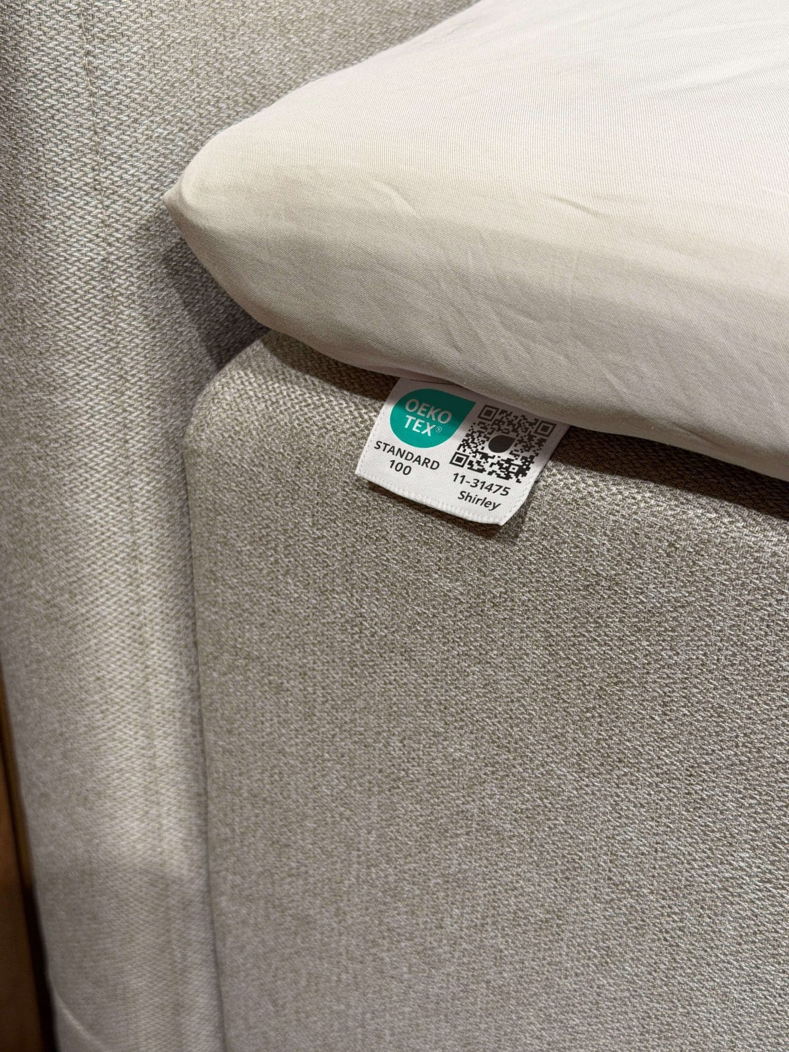 OEKO-TEX® STANDARD 100 label sewn onto the bed's beige fabric beneath the sheet