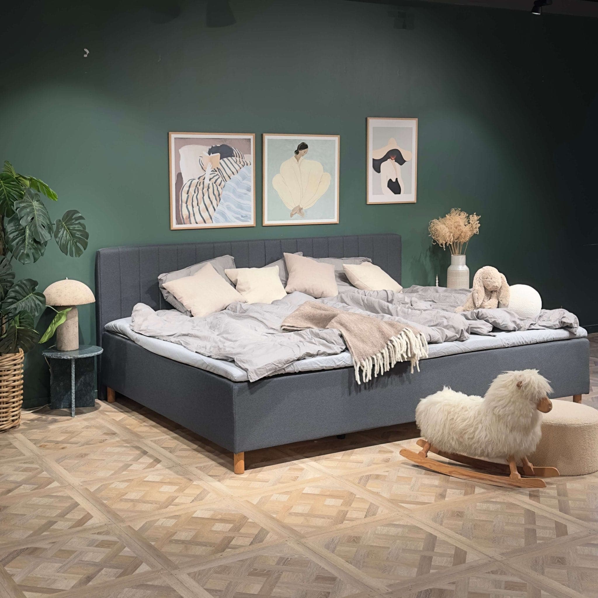 Wide, made-up grey family bed in a bedroom with a green wall and a rocking sheep on the floor