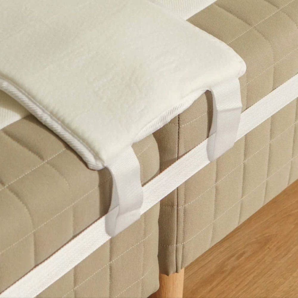 White mattress wedge placed over the join between two mattresses and held in place by the bed strap