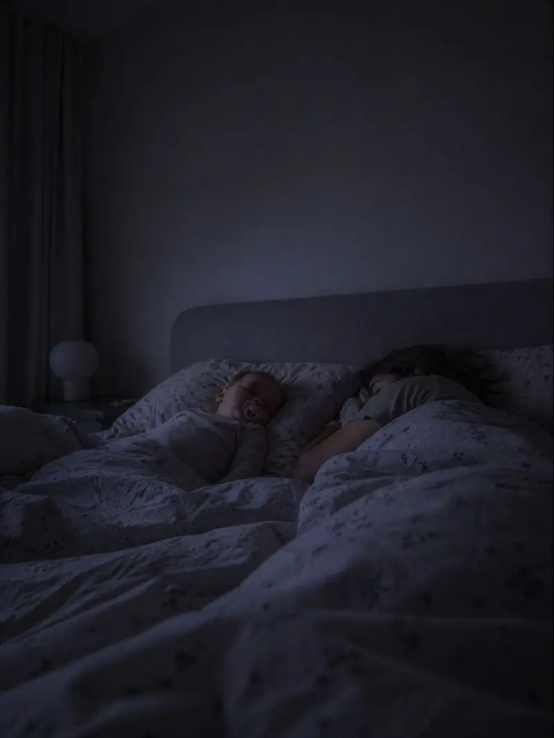 Parents and a child sleeping close together in bed in soft, low light at night